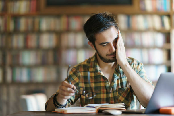 istock Tired young man rubbing his eyes at the library 1390788186