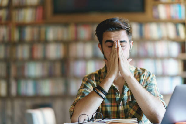 istock Tired young man rubbing his eyes at the library 1390788235