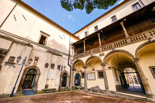 A suggestive view of the courtyard and the porch of the Palazzo dei Priori in the medieval heart of Viterbo. Built in 1264 as the seat of the local government, the Palazzo de Priori was then also used as the seat of the Pontifical Government, assuming its current Renaissance-style structure in 1460. Currently the Palazzo dei Priori is the seat of the municipal government of Viterbo. The medieval center of Viterbo, the largest in Europe with countless historic buildings, churches and villages, stands on the route of the ancient Via Francigena (French Route) which in medieval times connected the regions of France to Rome, up to the commercial ports of Puglia, in southern Italy, to reach the Holy Land through the Mediterranean. Located about 100 kilometers north of Rome along the current route of the Via Cassia, Viterbo is also known as the city of the Popes, because in the 13th century it was the Papal See for 24 years. Founded in the Etruscan era and recognized as a city with a papal document from the year 852 AD, the entire city is characterized by its stone and tuff constructions, materials abundantly present in this region of central Italy and which have always been used for the construction of houses and churches. Super wide angle image in high definition format.