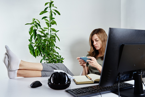 Woman procrastinate ar remote work. Freelancer use smartphone at home office. Unproductive office worker