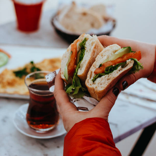 sándwich de desayuno por la mañana, té negro (té turco), tomate de pepino y sándwich de verduras, persona que come sándwich, sándwich de mano humana, persona que come en el café - sandwich turkey chicken submarine sandwich fotografías e imágenes de stock