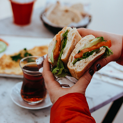 morning breakfast sandwich, black tea (turkish tea), cucumber tomato and vegetable sandwich, person eating sandwich, human hand holding sandwich, person eating in cafe