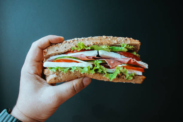 sandwich au petit-déjeuner du matin, sandwich à la tomate au concombre et aux légumes, sandwich à la personne mangeant, sandwich tenant la main humaine, sandwich sur pain de blé entier - sandwich submarine sandwich ham bun photos et images de collection
