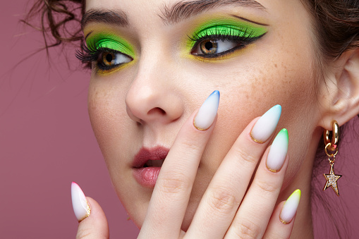 Portrait of young woman with hand near face. Female with unusual green eyes shadows makeup. Girl with nails with multi-colored manicure.