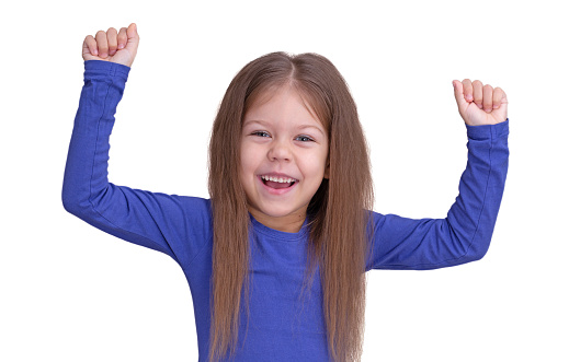 Isolated waist up caucasian happy lucky child kid little girl of 5 years in blue raising hands up on white background looking at camera