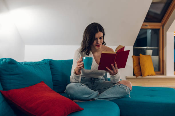 istock Woman reading a book and drinking tea while relaxing on a sofa at home 1390801389