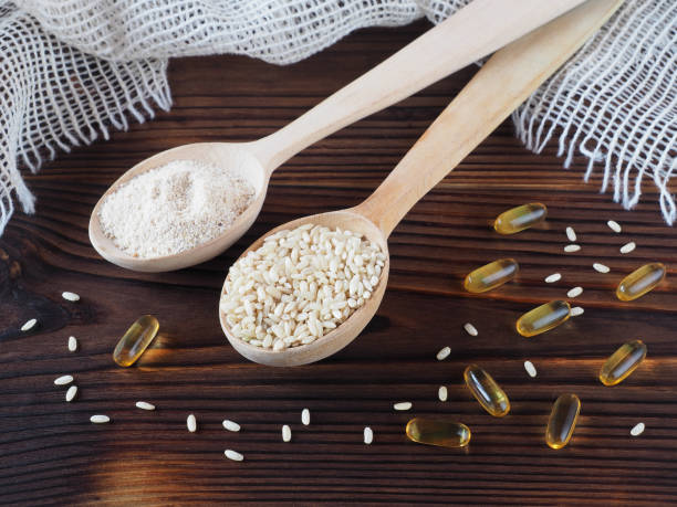 brauner roher reis und kleie in einem holzlöffel, reiskleieöl in kapseln, serviette auf einem dunklen holztisch, flacher grundriss. nützliche oryza-pflanzen mit omega und vitaminen für die vegetarische ernährung - lecithin capsule brown vitamin pill stock-fotos und bilder