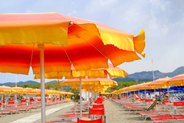 orange sun umbrella on the beach across blue sky, shining sun and mountains. Summer vacation background. Copy space orange sun umbrella on the beach across blue sky, shining sun and mountains. Summer vacation background. Copy space beach umbrella photos stock pictures, royalty-free photos & images