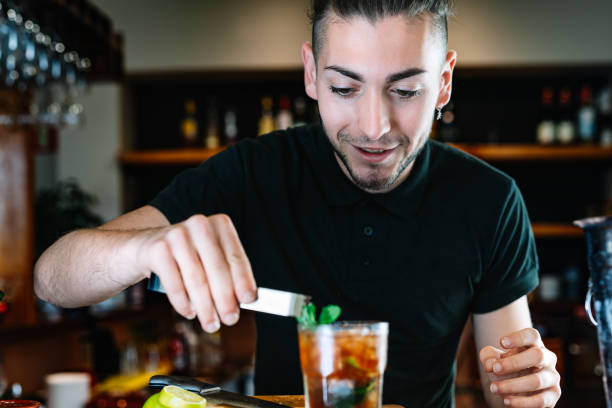 istock Young smiling waiter, putting mint leaves to decorate a cocktail. Horizontal 1390804740