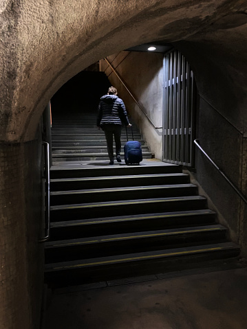 Woman travelling alone on Lisbon subway pictured walking up dark stairway with luggage.