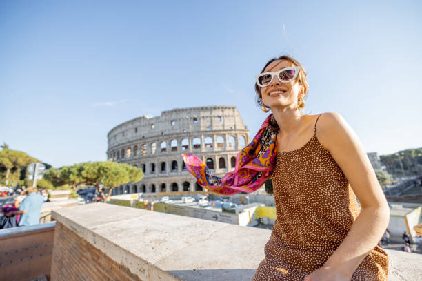 Portrait of a cheerful woman on background of Coliseum in Rome on a summer time. Concept of visiting famous landmarks and travel Italy. Girl wearing dress and colorful shawl