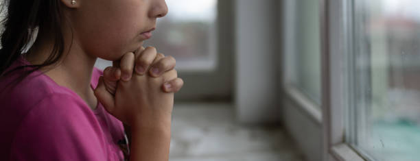 istock Praying little girl near window 1390808034
