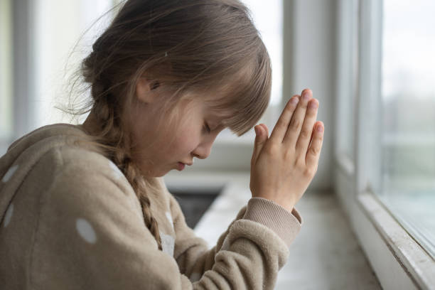 istock Praying little girl near window 1390808149