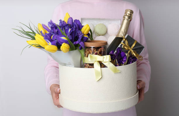 ライトグレーの背景にプレゼント、花束、シャンパンの入ったバスケットを持っている女性、クローズアップ - single flower bouquet flower holidays and celebrations ストックフォトと画像