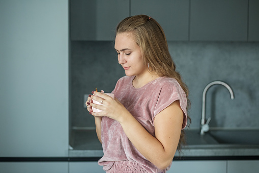 White cup with delicious hot tea. Modern gray kitchen interior. Vacation and lifestyle concept. Cozy house. Long curly hair.