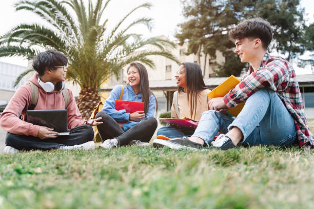 group of multiracial international exchange university student friends sitting on the grass in the college campus - campus imagens e fotografias de stock