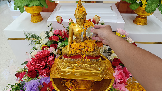 Songkran Thai woman pours water on a golden Buddha image with her hands