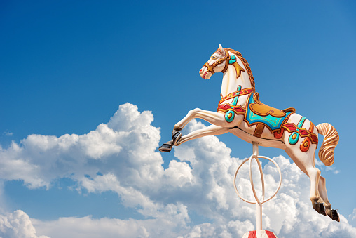 Close-up of a Carousel Horses or Merry-go-round against a beautiful clear blue sky with clouds and copy space. Italy, Europe.