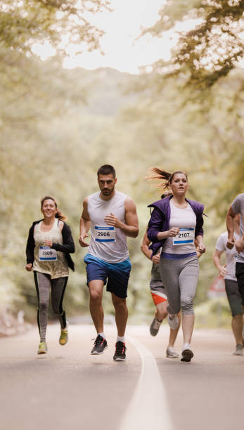 Group of people running a marathon on asphalt road in nature. Group of athletes running a marathon through nature. Copy space. distance running stock pictures, royalty-free photos & images