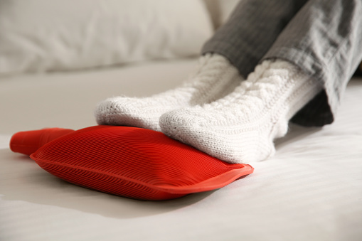 Person warming feet with hot water bottle on bed, closeup