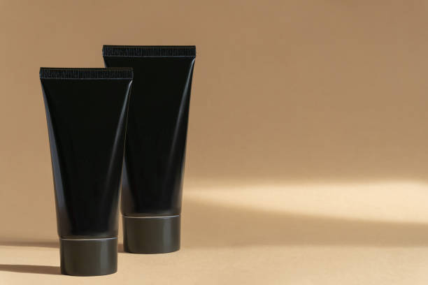 two dark plastic tubes with cream for face, hands and body on beige background with abstract shadow. unmarked containers with shaving foam, gel in morning sun. concept of men's skin care - shampoo merchandise packaging razor imagens e fotografias de stock