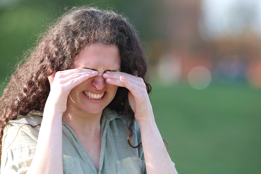 Stressed woman scratching itchy eyes in a park