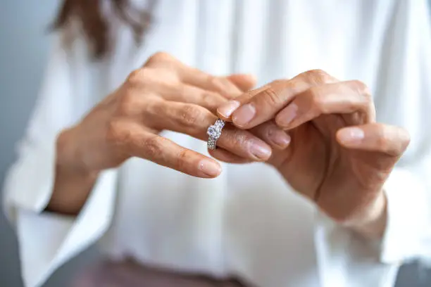 Photo of Unhappy woman holding wedding ring close up