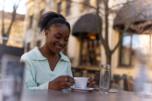 Afro american woman sitting in outdoor caffe and drinking coffe