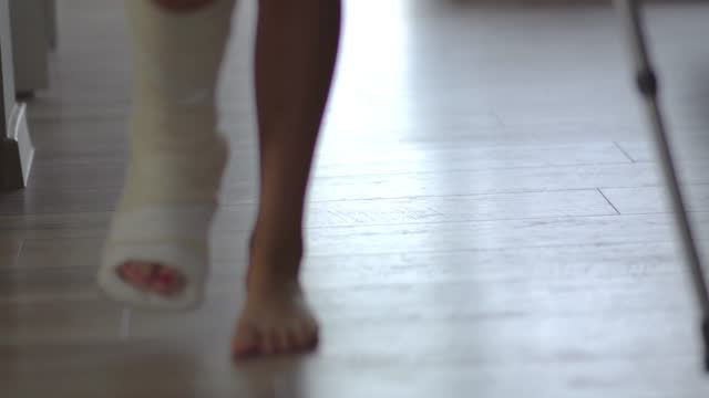 Jeune femme avec la jambe cassée en plâtre essayant de marcher avec des  béquilles dans le salon. Blessure physique, fracture osseuse et accident,  Clip Vidéo 1390825810