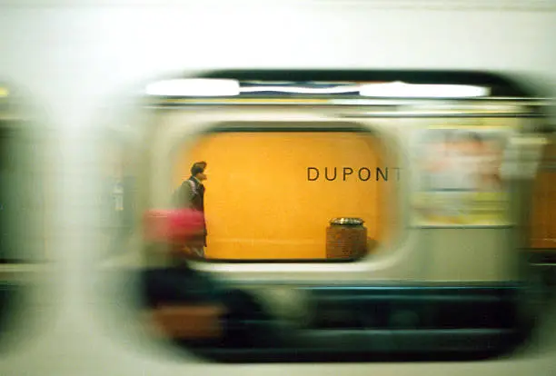 Looking through a subway car of the Toronto subway system as it blurs past and someone walks towards the 'DUPONT' station name sign.