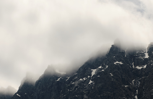The cloud is stuck in the snowy rocky peak of the high mountain. Air element. Wind, clouds, bad weather, before storm, dangerous climbing theme. Concept of climate. landscape photo for wallpaper, poster