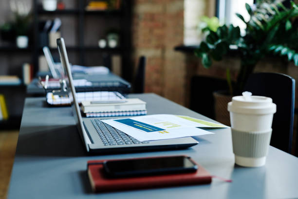 Cup of coffee, notebook, smartphone, laptop with financial documents on keyboard on workplace of contemporary economist