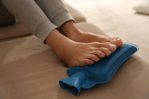 istock Man warming feet with hot water bottle on sofa, closeup 1390829157