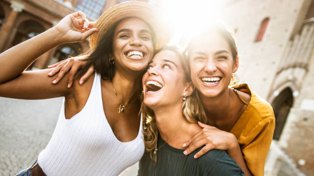 tre giovani donne multirazziali che si divertono per strada all'aperto - amiche di razza mista che si godono una giornata di vacanza insieme - stile di vita felice, concetto di giovani e giovani donne - town of friendship foto e immagini stock