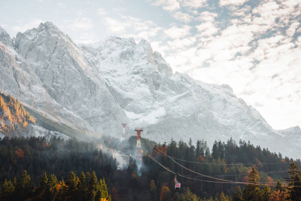 alpine ropeway lifting passengers up to the top of Zugspitze small red cable car on the alpine ropeway lifting passengers up to the top of Zugspitze. Smoke in mountain forest near cableway zugspitze stock pictures, royalty-free photos & images