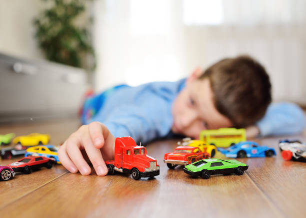 small child preschool boy playing toy cars on the wooden floor in a bright room stock photo