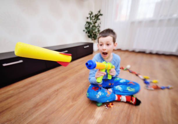 a small hyperactive child preschool boy shoots foam bullets from a toy gun weapon. Flight of a toy bullet close-up against the background of a bright room.