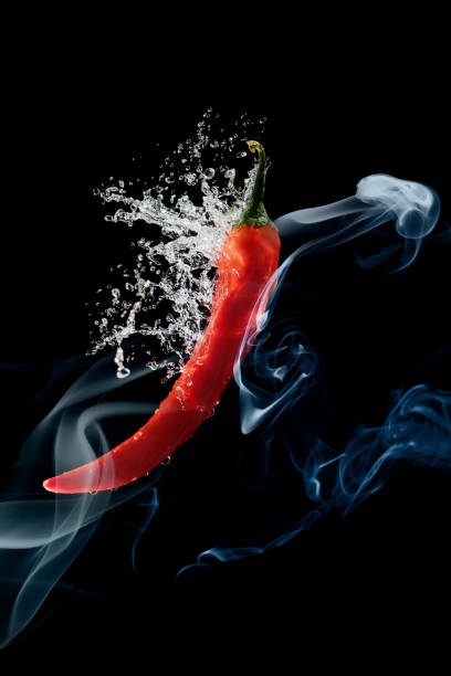 Red pepper  in water splash and smoke over black background