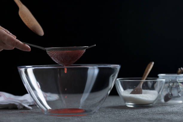 Woman straining strawberry jam through a sieve