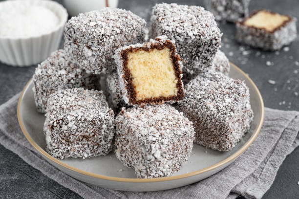 gâteau lamington australien traditionnel dans un glaçage au chocolat et des flocons de noix de coco sur une assiette sur fond de béton gris avec une tasse de thé. mise au point sélective. - lamingtons photos et images de collection