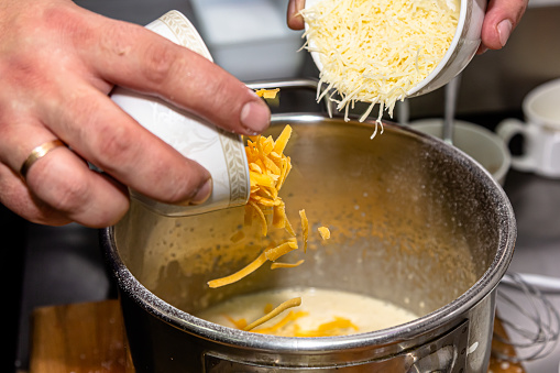 The cook adds grated cheese to the cheese sauce