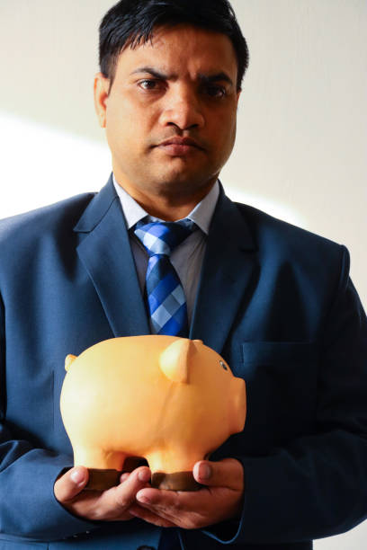 Stock photo showing close-up view of ceramic piggy bank held by Indian business man. Banking and finances concept.