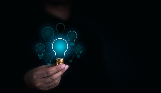 Creative idea management, solution, innovation, knowledge technology, and inspiration concept. Glowing blue light bulbs graphics with blank space inside in human hand on dark background.