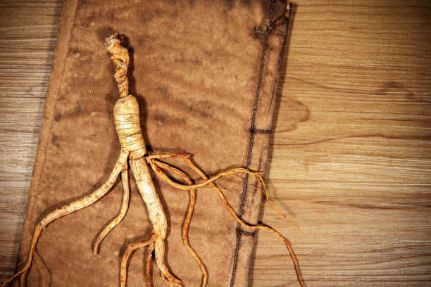 istock Dried ginseng root and ancient book on wood background 1390846867