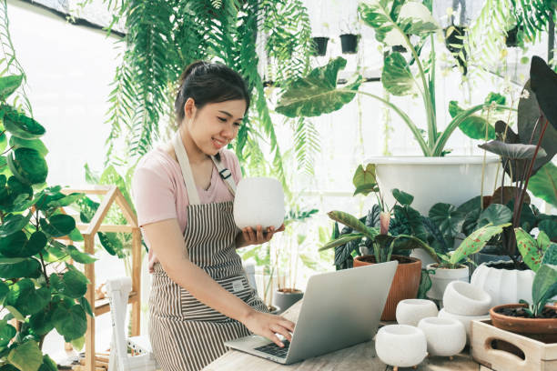 молодая женщина владелец магазина растений проверяет заказ клиента с сайта - farmer laptop selling internet стоковые фото и изображения