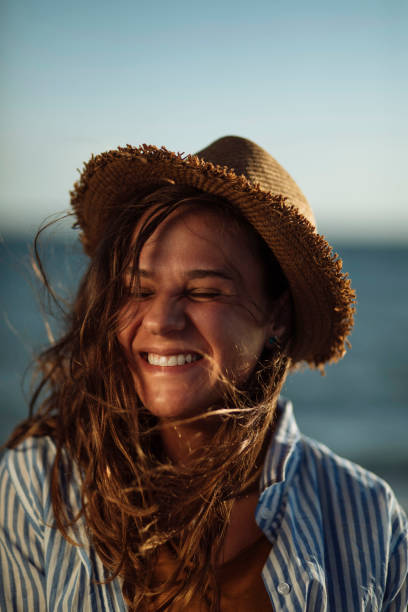 Portrait of beautiful smiling young woman wearing straw hat at beach with sea in background