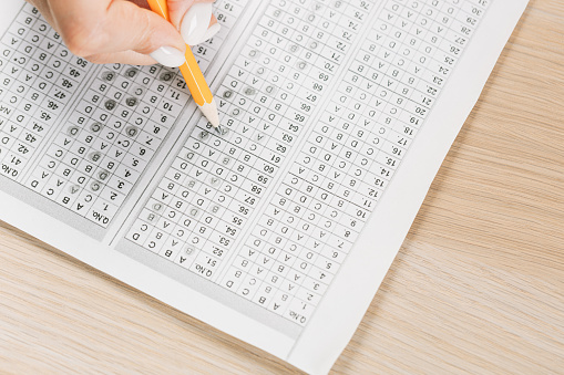 Students hands to take exams, writing an exam room with a pencil holding on an optical form of a standardized test with answers and an English piece of paper on a row chair to do the final exam in the classroom.