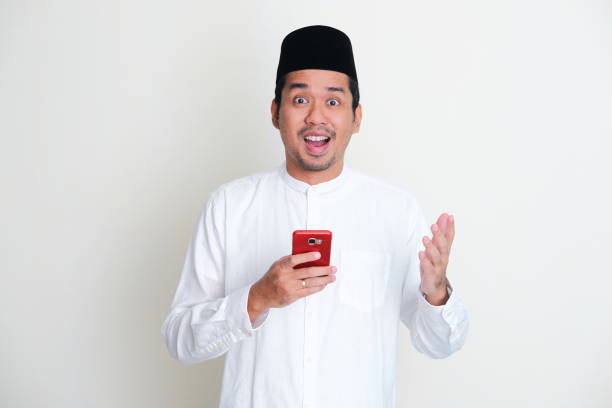 istock Moslem Asian man showing amazed expression while holding mobile phone 1390852007