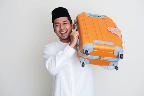 Moslem Asian man smiling happy while carrying travelling suitcase Moslem Asian man smiling happy while carrying travelling suitcase keluarga stock pictures, royalty-free photos & images