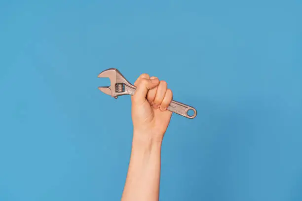 Photo of Woman's hand with an adjustable wrench against blue background